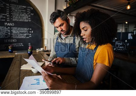 Occupied Business Co-workers Sorting Out Bank Statements For The Week Working At Trendy Coffee Shop