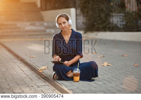 Cute Student Girl Sitting On Ground And Studying. Headset And Modern Tablet. Distance Learning And S