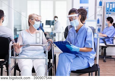 Disabled Woman Using Walking Frame In Hospital Waiting Room Wearing Face Mask Against Coronaviurs Ha