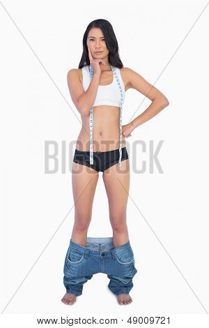 Eftertænksom kvinde iført jeans falder ned, fordi shes mistede vægt på hvid baggrund