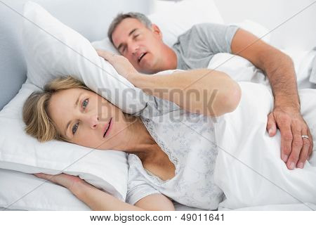 Irritada esposa bloqueando sus oídos del ruido de esposo roncando en dormitorio en casa
