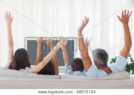 Famiglia guardando la televisione e aumento delle braccia sul divano