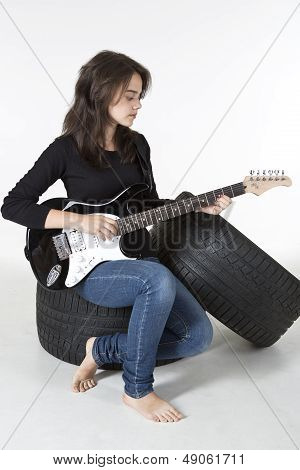 Teenager is sitting on old tire and playing guitar