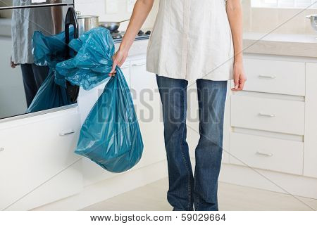 Low section of a young woman carrying garbage bag in the kitchen at house