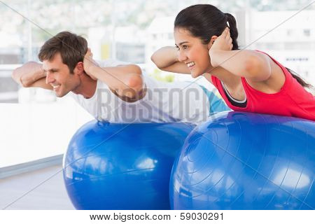 Fit young couple exercising on fitness balls in the bright gym