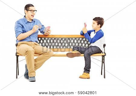 Young boy playing cards with his older cousin seated on bench isolated on white background