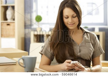 Young woman sitting at table at home, using mobilephone.