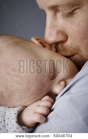 Closeup photo of father kissing sleeping newborn baby's face.