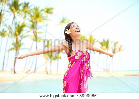 Happy woman praising freedom smiling on hawaiian palm beach in sarong, arms stretched out. Beautiful mixed race female model enjoying sun in worship and meditation zen. Big Island, Hawaii, USA.