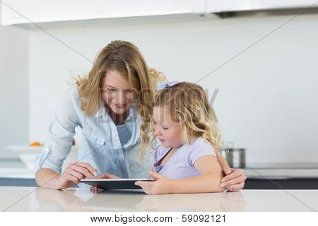 Woman and daughter using tablet computer together at table in kitchen