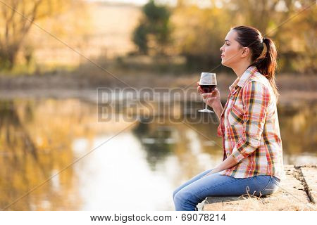 thoughtful young woman with glass of wine on pier in autumn
