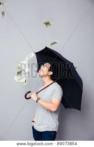 Asian man standing in the rain of money over gray background