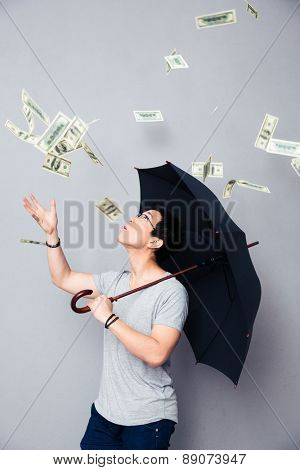 Asian man standing with umbrella in the rain of money over gray background