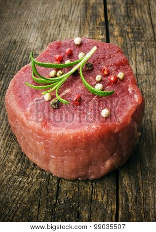 raw steak with pepper and rosemary on the wooden background