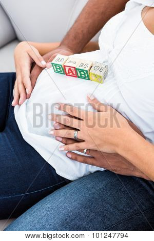 Midsection of pregnant woman belly with toy sitting on sofa at home