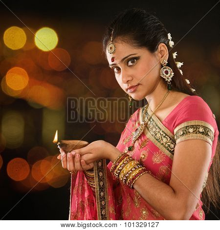 Indian girl in traditional sari lighting oil lamp and celebrating Diwali or deepavali, fesitval of lights at temple. Female hands holding oil lamp, beautiful lights bokeh background.