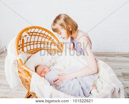 Little baby sleeps in cradle and her older sister looking at her