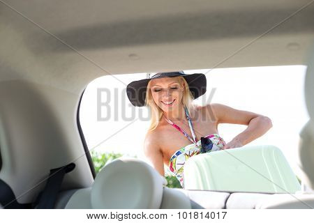 Happy woman loading suitcase in car trunk