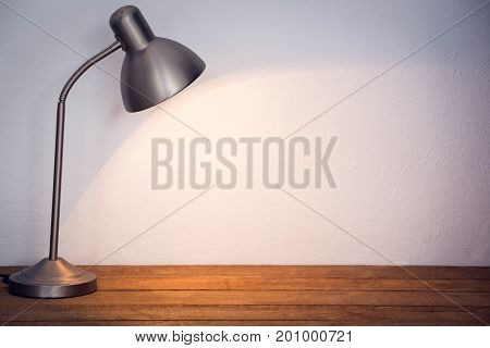Illuminated table lamp on wooden table by wall in office