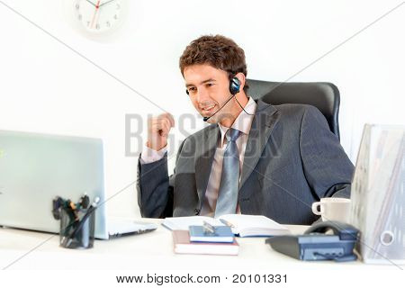 Sourire homme d'affaires moderne avec casque assis au bureau et à la recherche sur ordinateur portable