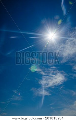Sun with lens flare on blue sky background. Glare from the bright sun in a clear blue sky with a little cloudiness and the effect of vignetting