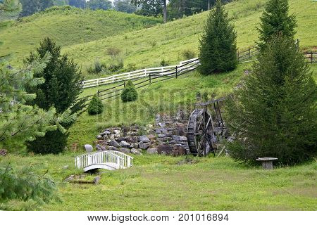a decorative waterwheel, white picket fence and footbridge