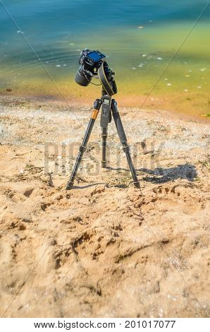 Camera on a tripod near the seaside removes of seashells on the sand. Photographic equipment in the process of shooting the landscape. Camera while taking a photo or time-lapse