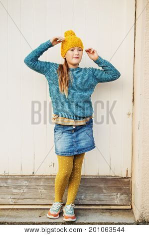 Outdoor fashion portrait of cute 9 year old little girl wearing yellow hat blue pullover denim skirt and polka dot tights