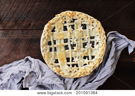 Top view of a blueberry pie with lattice and stars crust over a rustic wooden background.