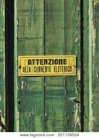 Attention alla corrente elettrica (High voltage in italian) sign on a weathered green wooden wall background texture.