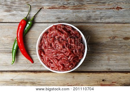 Raw Meat stuffing in a white bowl on a wooden table, top view, rural style