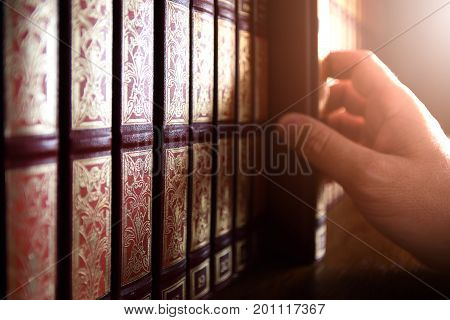 Professional library manager picking up an encyclopedia book from the shelve in a dark room. Back light and empty copy space for Editor's text..