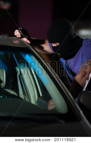 Closeup of dangerous criminal man pointing gun at the driver. Car theif threatening frightened driver, night time.