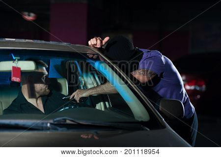 Aggressive man thief threatening with gun to frightened auto owner on car parking. Car theft, night time