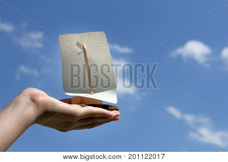 Homemade sailboat on hand against the sky with clouds / tailwind for your dreams