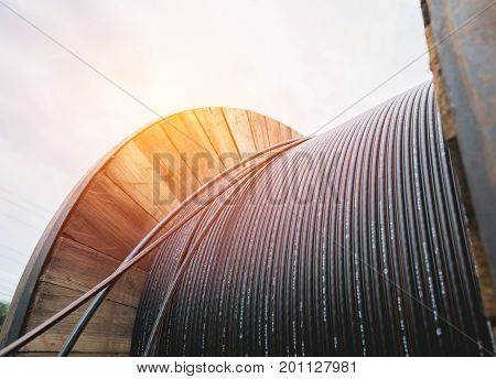 black wire electric cable with wooden coil of electric cable under the sky.