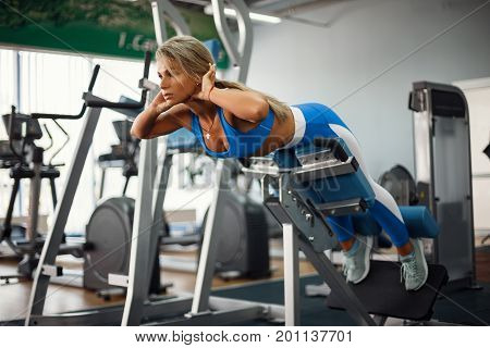 Athletic young woman doing hyperextension in the gym. Woman flexing back and abdominal muscles on bench