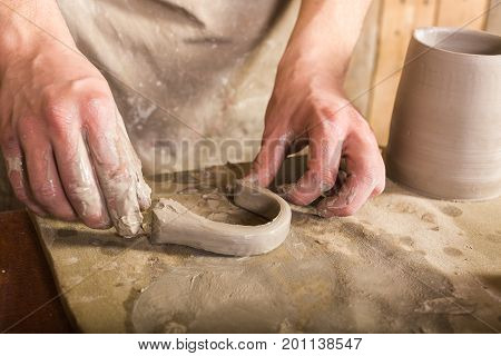 potter, stoneware, ceramics art concept - craftsman fingers forming the handle from raw fireclay, master hands working with some piece of clay, male stand at a workshop near the table