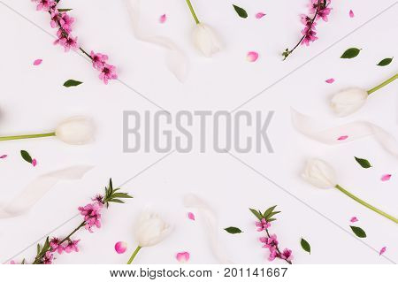 valentine day, spring, anniversary concept. on white desk there are magnificent tender flowers, creamy tulips, flowered brunches of cherrytree and ribbons. with negative space for text in the center