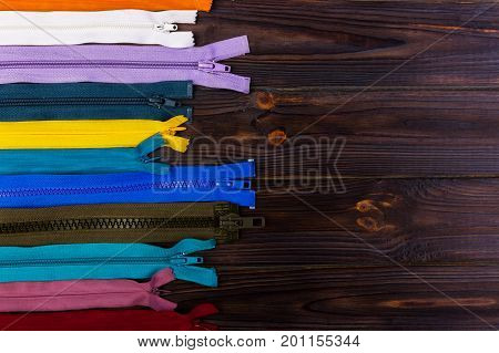 Multicolored zippers are laid out on a wooden table