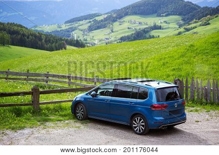 Val Di Funes, Italy - May 20, 2017: Blue Volkswagen Touran car is parked near green meadow in Funes Valley