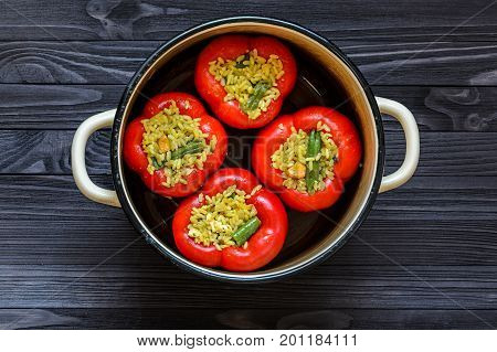 Four red stuffed peppers in a yellow saucepan on dark rustic kitchen table background top view. Cooking process
