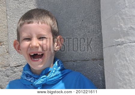 A gloomy boy with milk teeth in a shirt and a bandage laughing on a sunny day.
