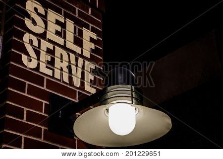 self serve sign on brick wall with light