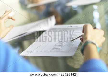 Woman in office, working with some sheets, pen and smartphone and pen in her hand. Blurred background.
