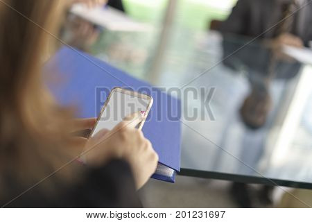 Woman in office, working with some sheets, pen and smartphone and pen in her hand. Blurred background.