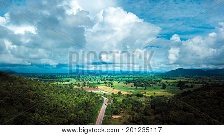 Aerial view of road going through countryside in between mountain and Blue Sky