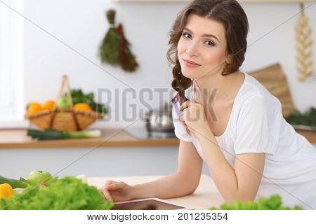 Young  woman looking for a new recipe for  cooking in a kitchen. Housewife is making online shopping by tablet computer and credit card.