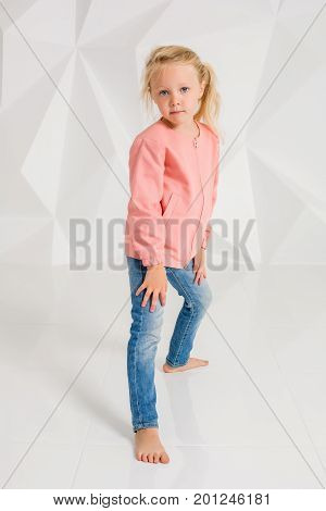 Cute little girl in pink jacket and jeans on white background. Little brunette posing in studio