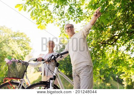old age, people and lifestyle concept - happy senior couple walking with fixie bicycles at summer city park